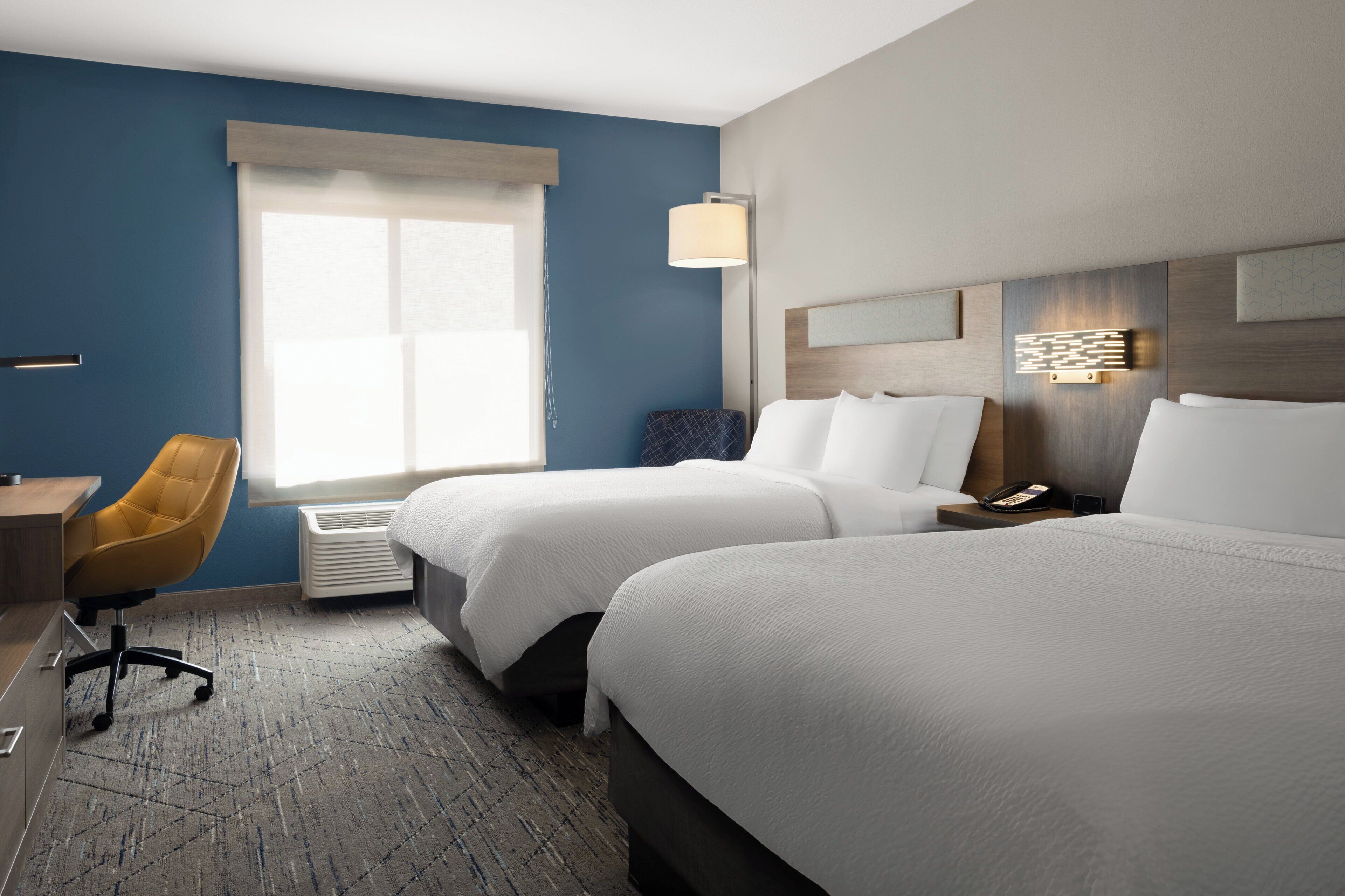 A hotel room with two beds, a desk, a chair, a lamp, and a phone on the nightstand.