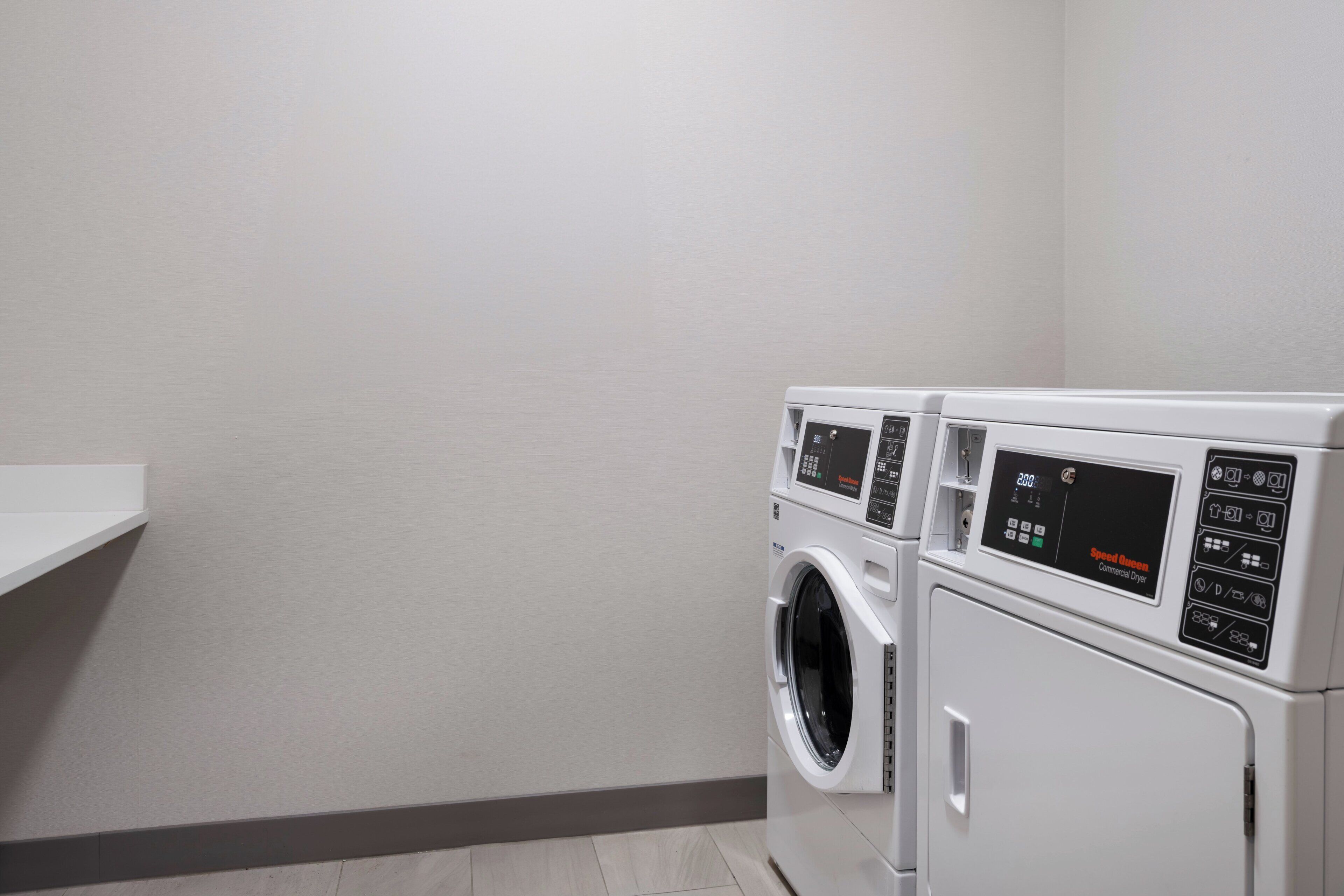 A laundry room with two front-loading washing machines and a white shelf.