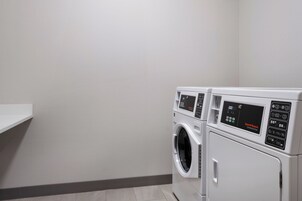 Una sala de lavandería con dos lavadoras de carga frontal y un estante blanco.