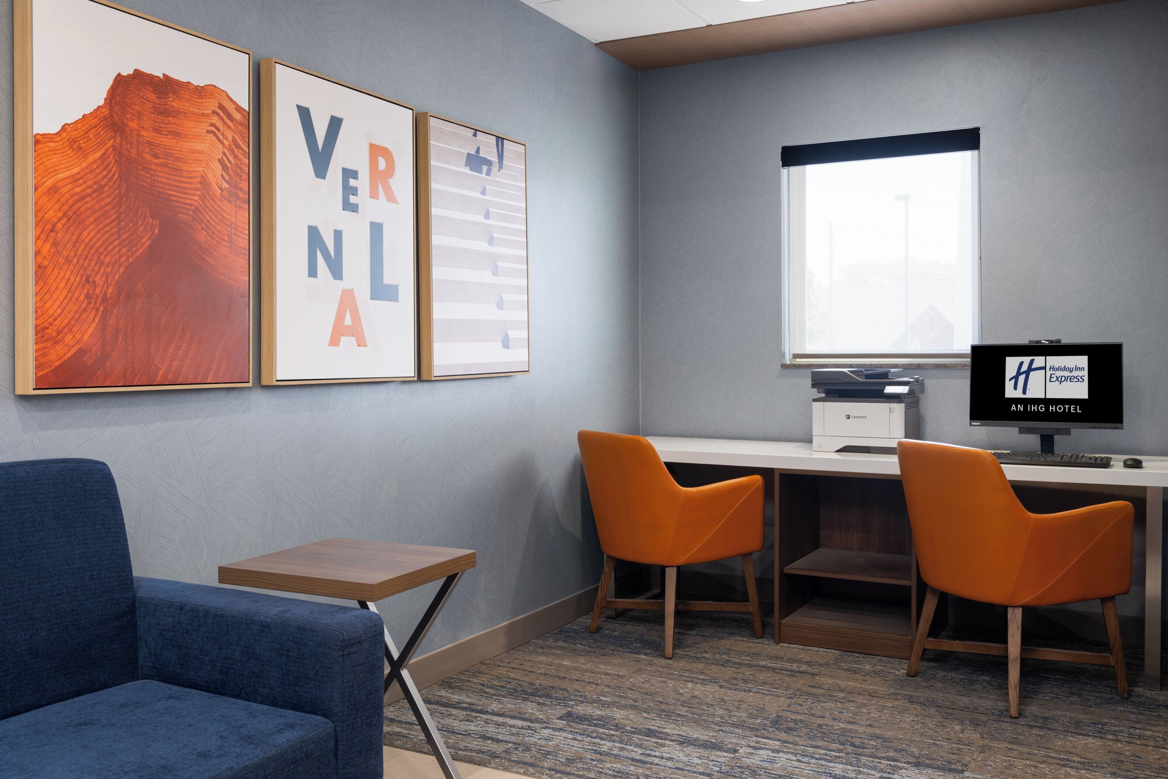 Habitación de hotel con escritorio, dos sillas, una computadora y cuadros en la pared.