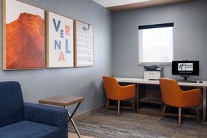 Habitación de hotel con escritorio, dos sillas, una computadora y cuadros en la pared.