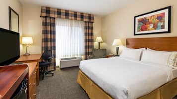 Habitación de hotel con cama, escritorio, silla, televisor, lámparas y un cuadro en la pared.