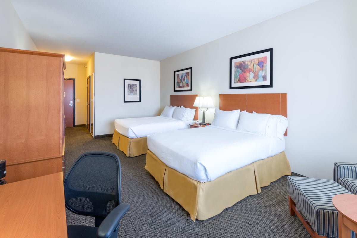 A hotel room with two beds, a desk, a chair, a small table, and a couch.