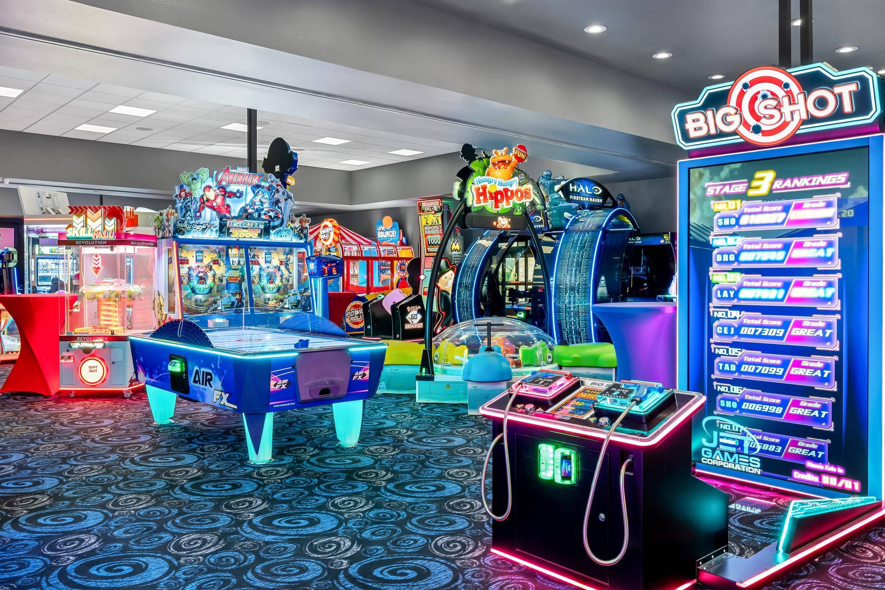 An indoor arcade with various gaming machines, including a pool table and a neon sign for 'BIG SHOT.'