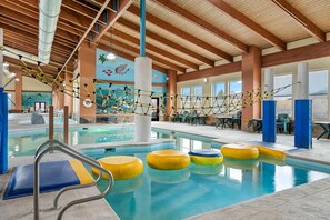 An indoor swimming pool with a rope bridge, yellow and blue floating rings, and a view of the mountains through large windows. - Big Horn Resort, an Ascend Collection Hotel (Billings)