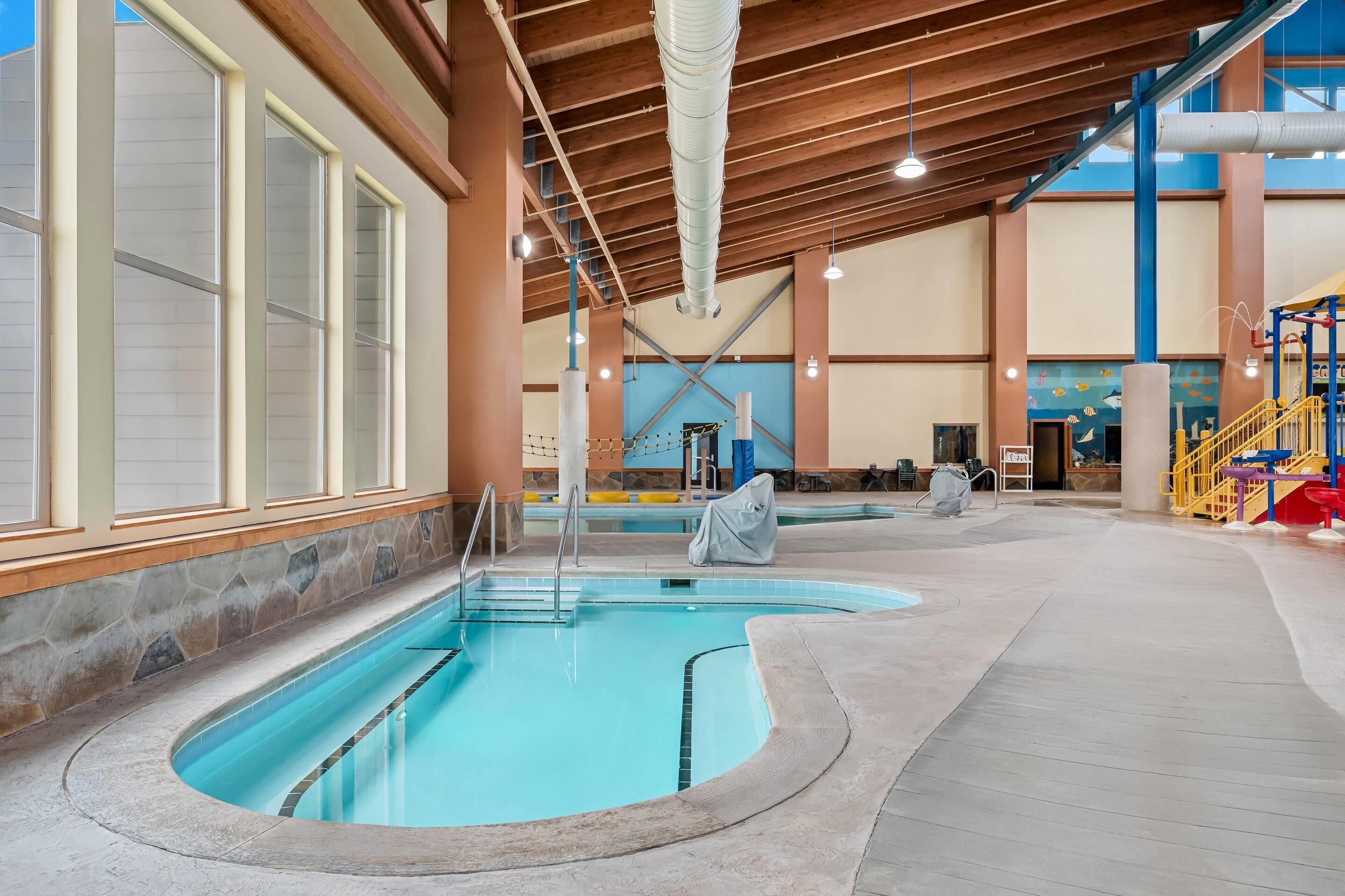Una piscina interna con parete in pietra, travi in legno e un'area giochi per bambini con uno scivolo.