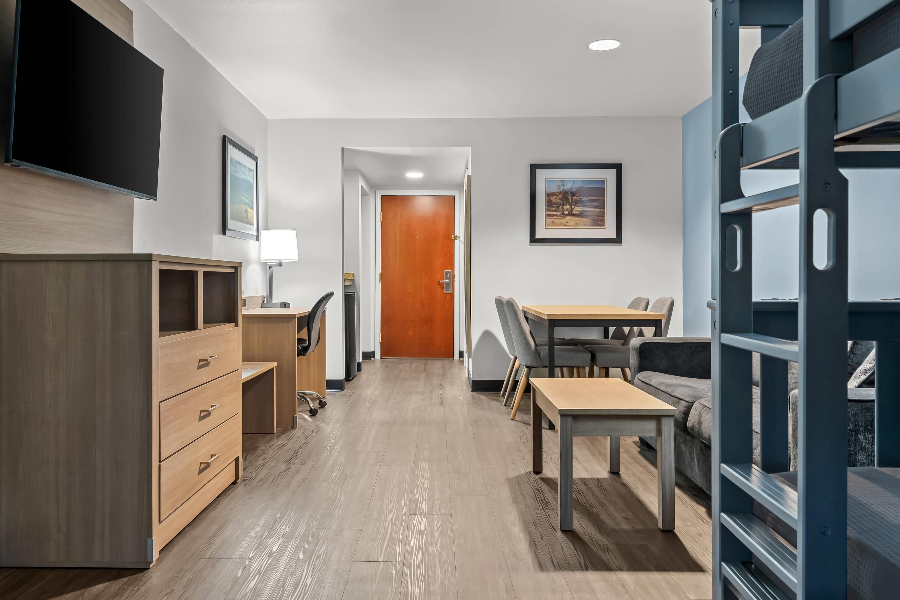 Habitación de hotel con un escritorio de madera, un sofá, una cama litera, un televisor y una puerta que da a otra habitación.