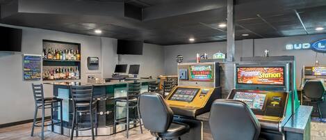 Un'area bar con sgabelli, un bancone e una jukebox, più un cartello luminoso al neon.