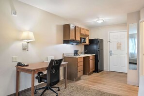 A compact kitchen with wooden cabinets, a microwave, a refrigerator, a small countertop, a chair, a desk, and a lamp. - Suburban Studios Waterloo (Waterloo)