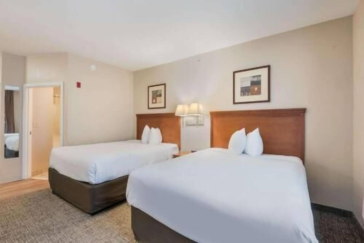 A hotel room with two beds, a door, and a wall-mounted lamp.
