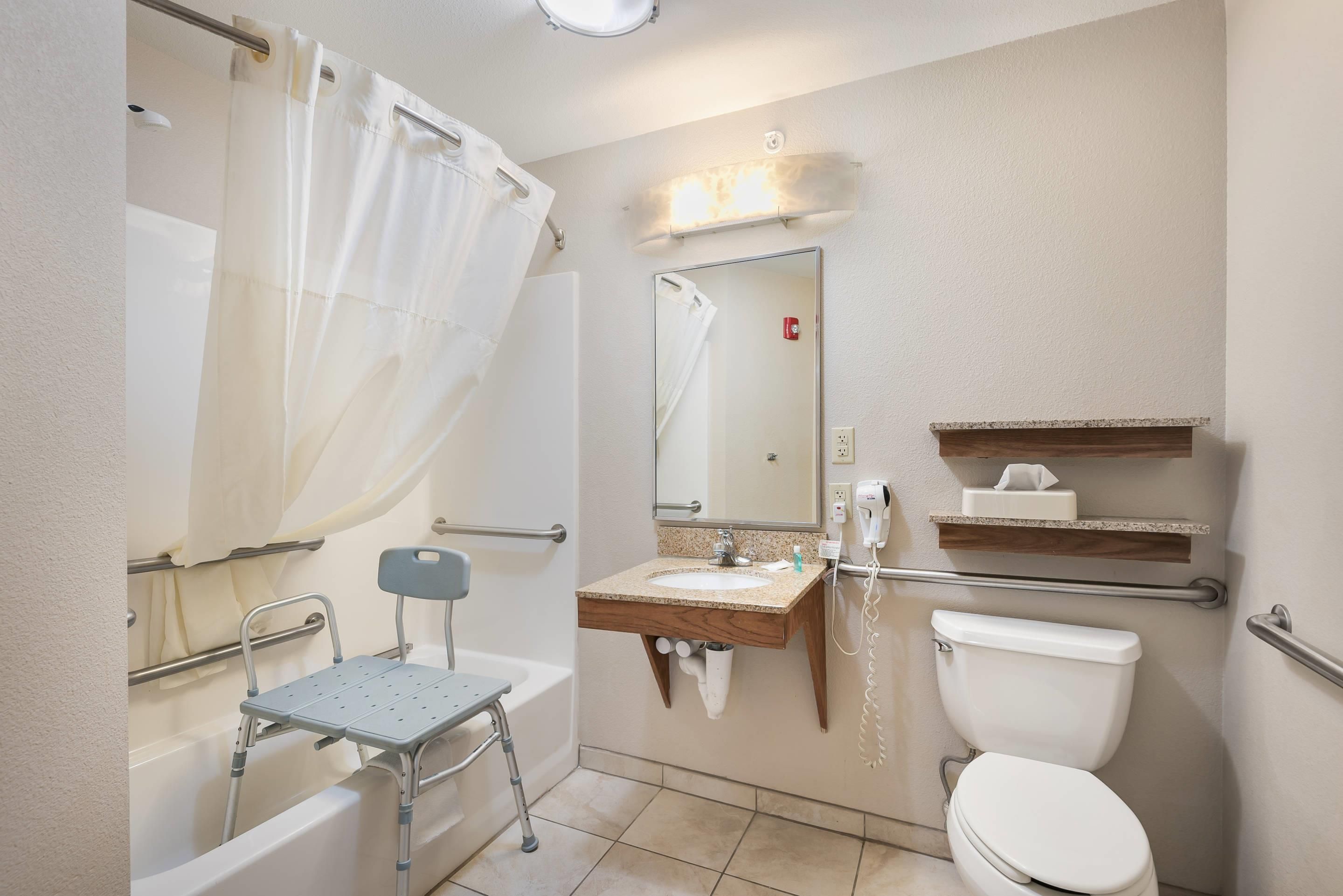 A bathroom with a shower, a toilet, a sink, a mirror, and a grab bar.