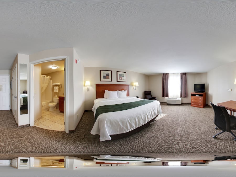 Quarto de hotel com cama, escrivaninha, cadeira e banheiro visível através de uma porta aberta.