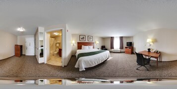 Habitación de hotel con cama, escritorio, silla y baño visible a través de una puerta abierta.