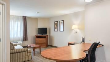 A hotel room with a sofa, a TV, a desk, a lamp, and a dining table.