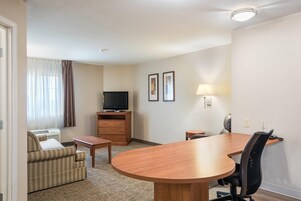 A hotel room with a sofa, a TV, a desk, a lamp, and a dining table.