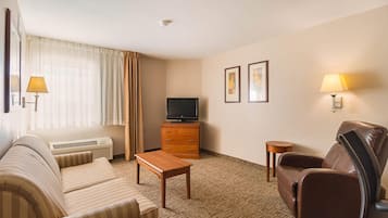 A hotel room with a sofa, a chair, a television on a wooden cabinet, a small table, and two wall-mounted lamps.