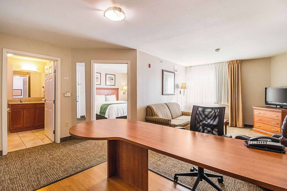 A hotel room with a large wooden desk, a television, a sofa, and a dining table.