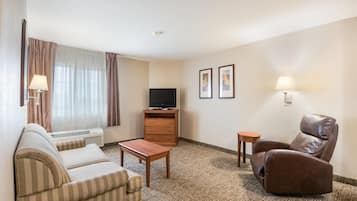 Een hotelkamer met een sofa, fauteuil, televisie en twee ingelijste foto's aan de muur.