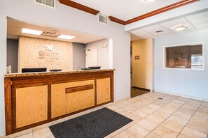 A reception area with a wooden counter, a stone wall with the text "QUALITY", and a tiled floor.