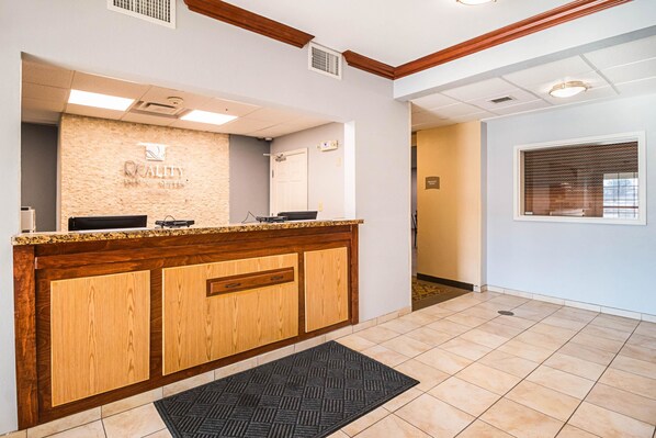 A reception area with a wooden counter, a stone wall with the text "QUALITY", and a tiled floor.