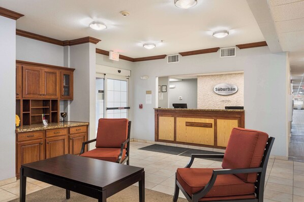 A lobby with a reception desk, wooden cabinets, and two red chairs. - Suburban Studios Waterloo (Waterloo)