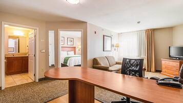 A hotel room with a large wooden desk, a television, a sofa, and a dining table.