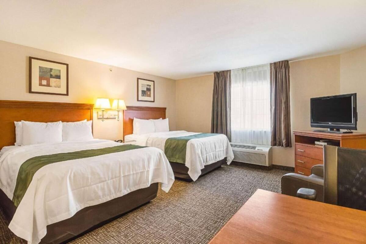 A hotel room with two beds, a desk, a television, and a window with curtains.