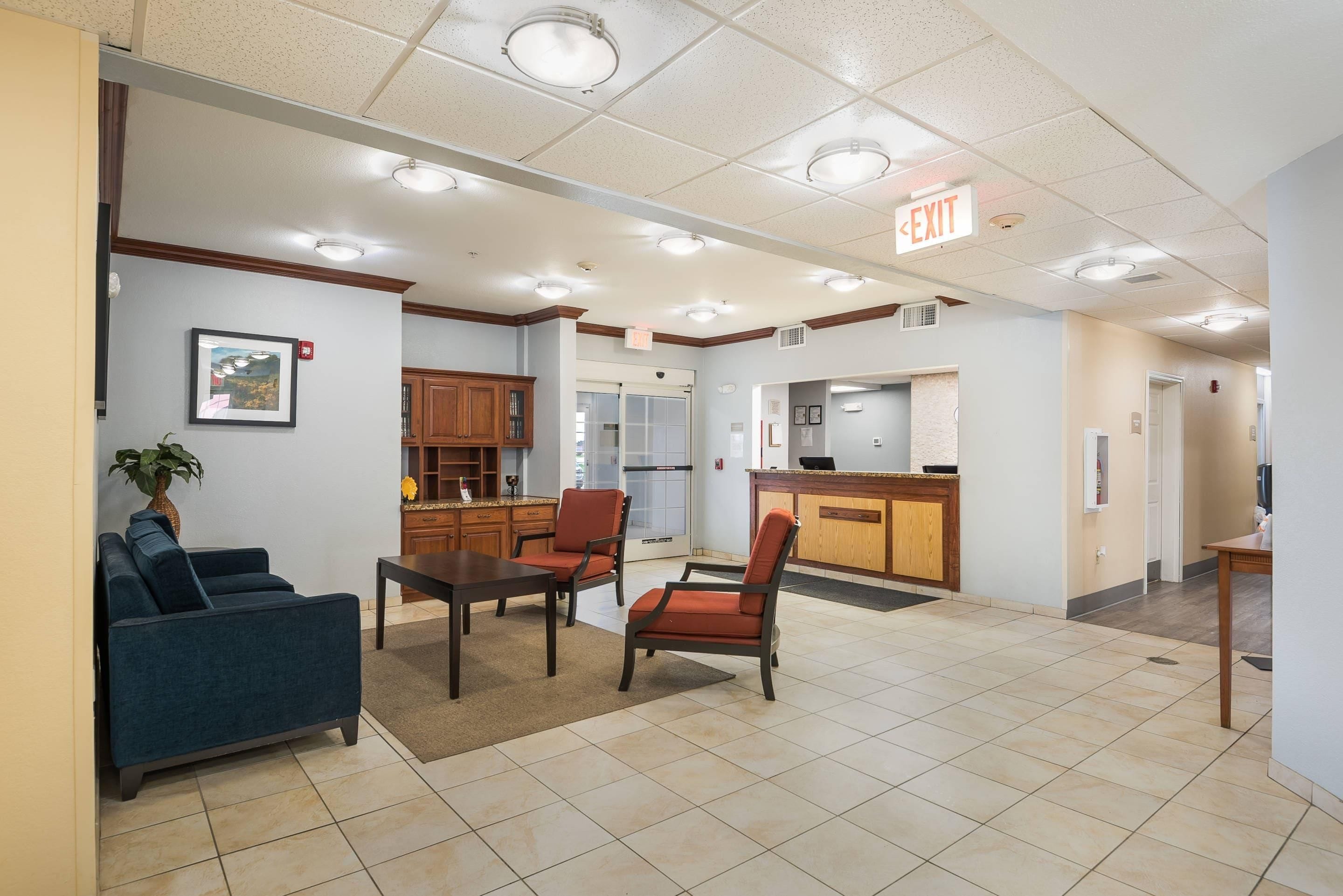 A hotel lobby with a reception desk, seating area, and a kitchenette.