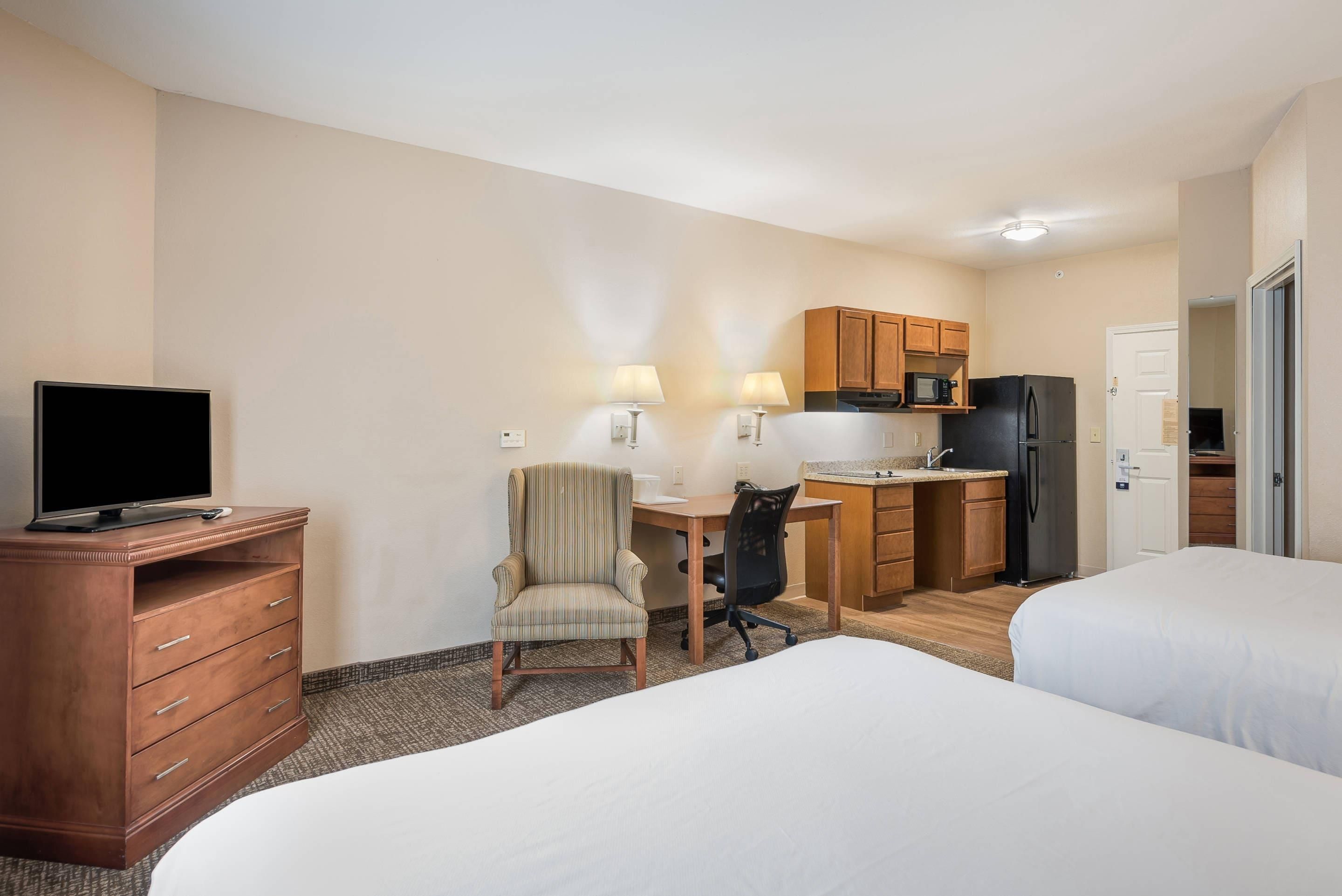 A hotel room with two beds, a desk with a chair, a kitchenette, and a TV on a dresser.