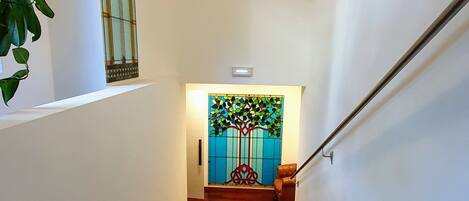 A wooden staircase leading to a door with a stained glass window depicting a tree.