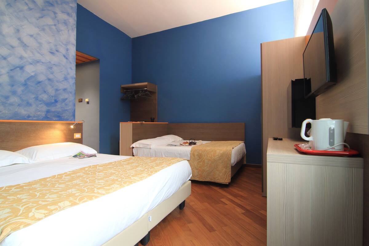 A hotel room with two beds, a wooden headboard, a flat-screen TV, a coffee maker, and a wooden cabinet.