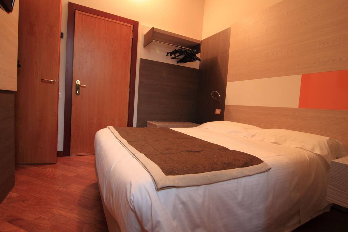 A bedroom with a bed, a wooden door, and a wall-mounted shelf with clothes.