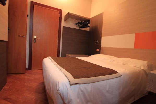 Un dormitorio con una cama, una puerta de madera y un estante en la pared con ropa.