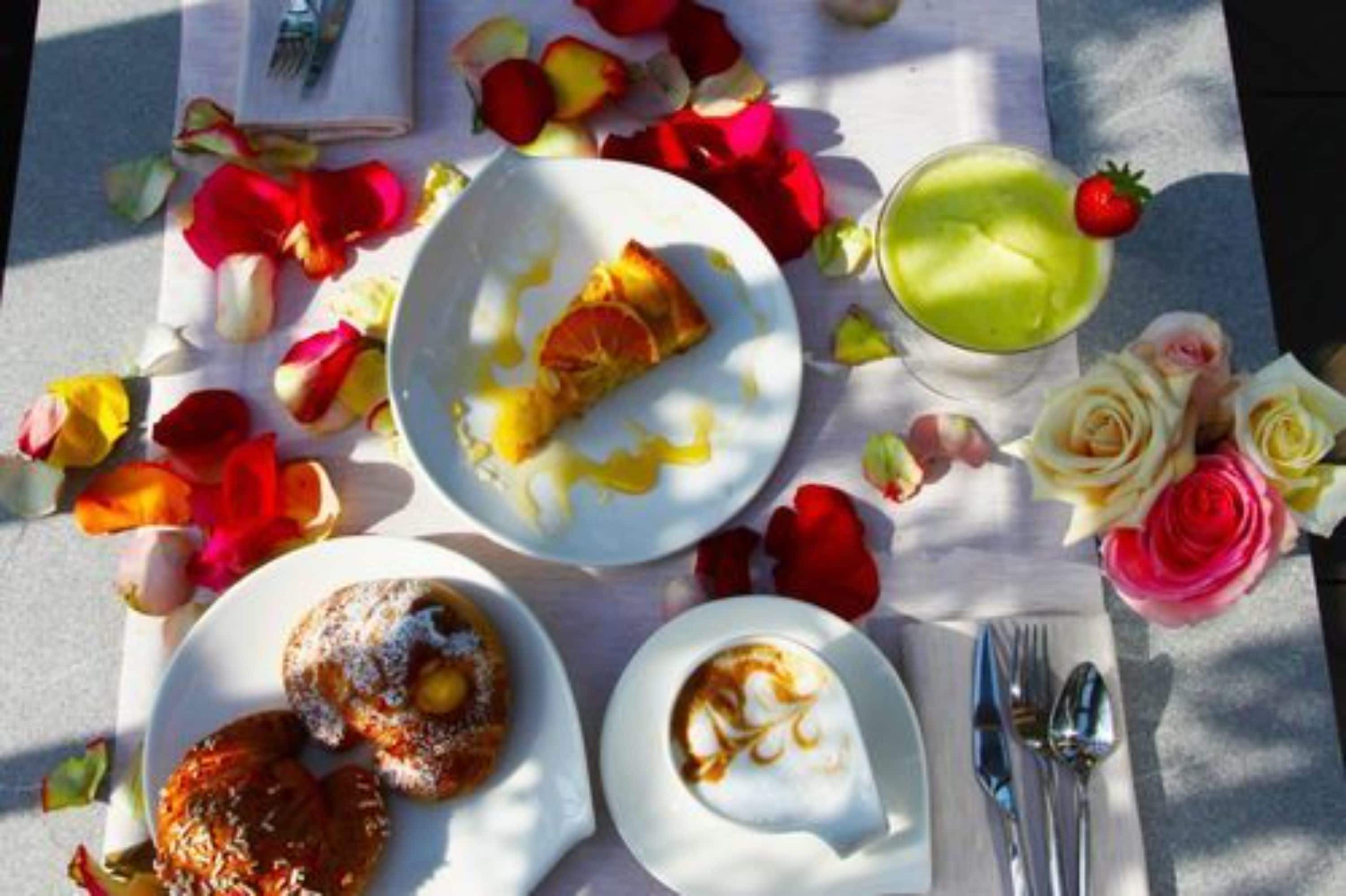 Una mesa servida con platos de comida, una bebida verde y pétalos de rosa esparcidos.