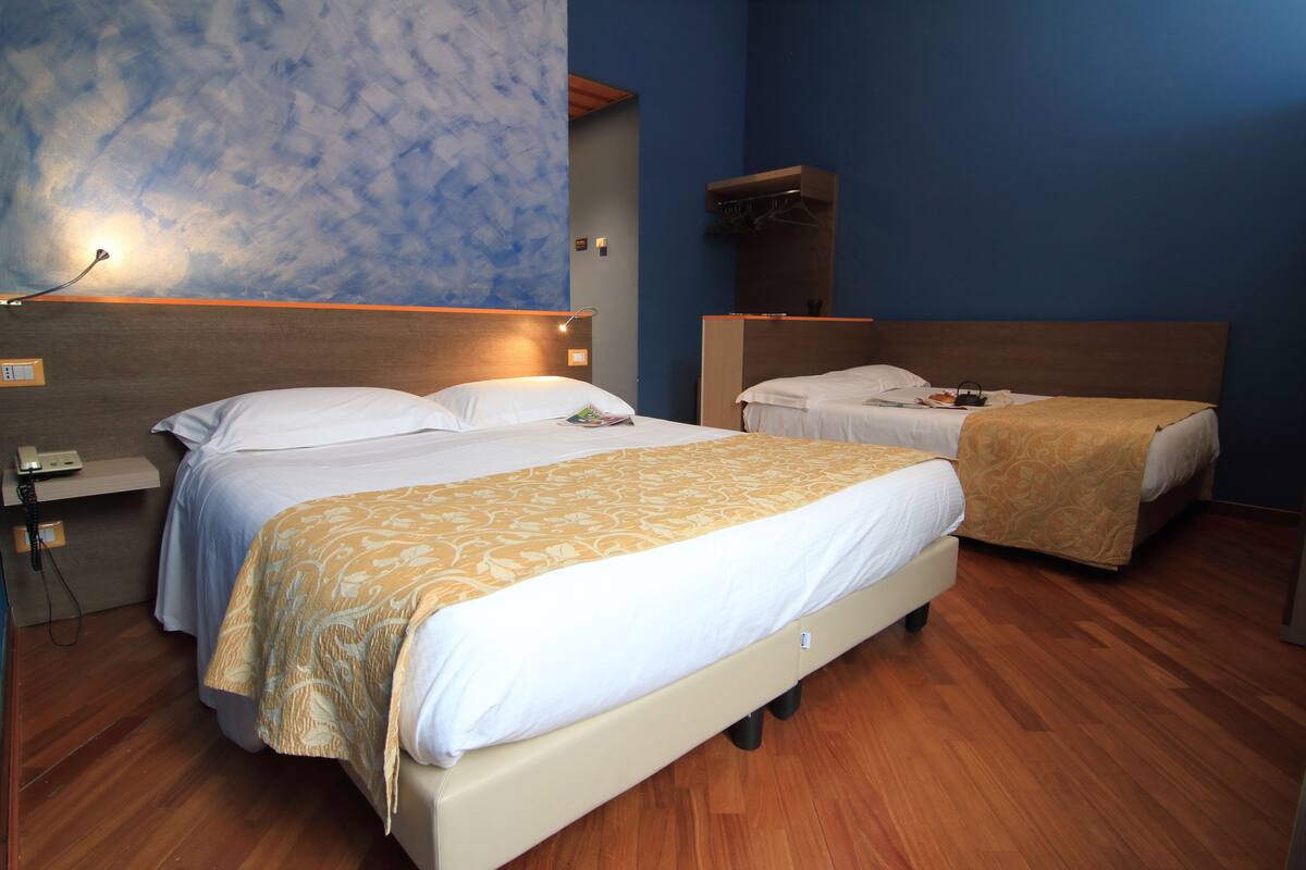 A hotel room with two beds, a wooden floor, a wall with a cloud pattern, and a nightstand with a phone.