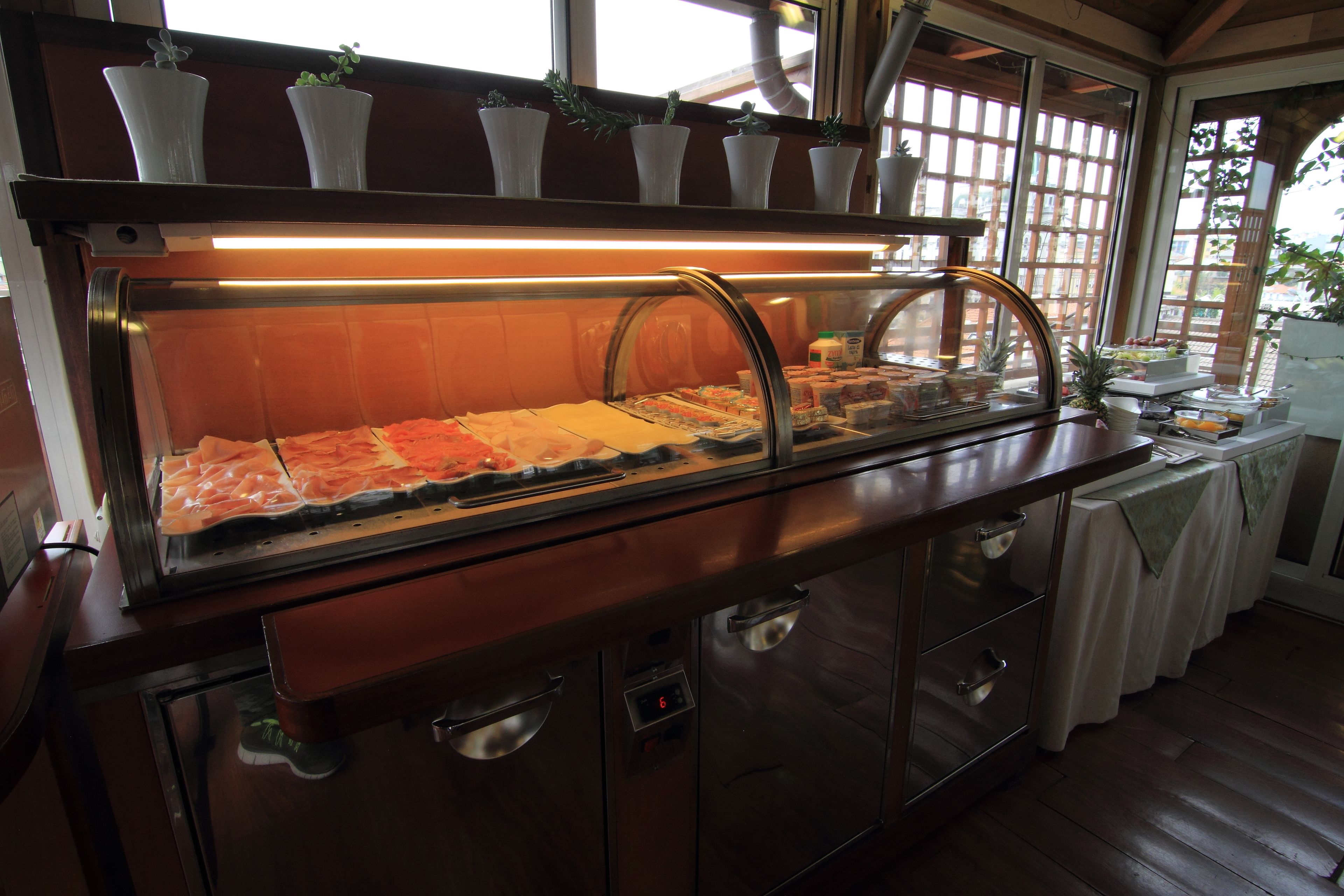 Un bufé con diversos alimentos, una vitrina de vidrio y una ventana con plantas.