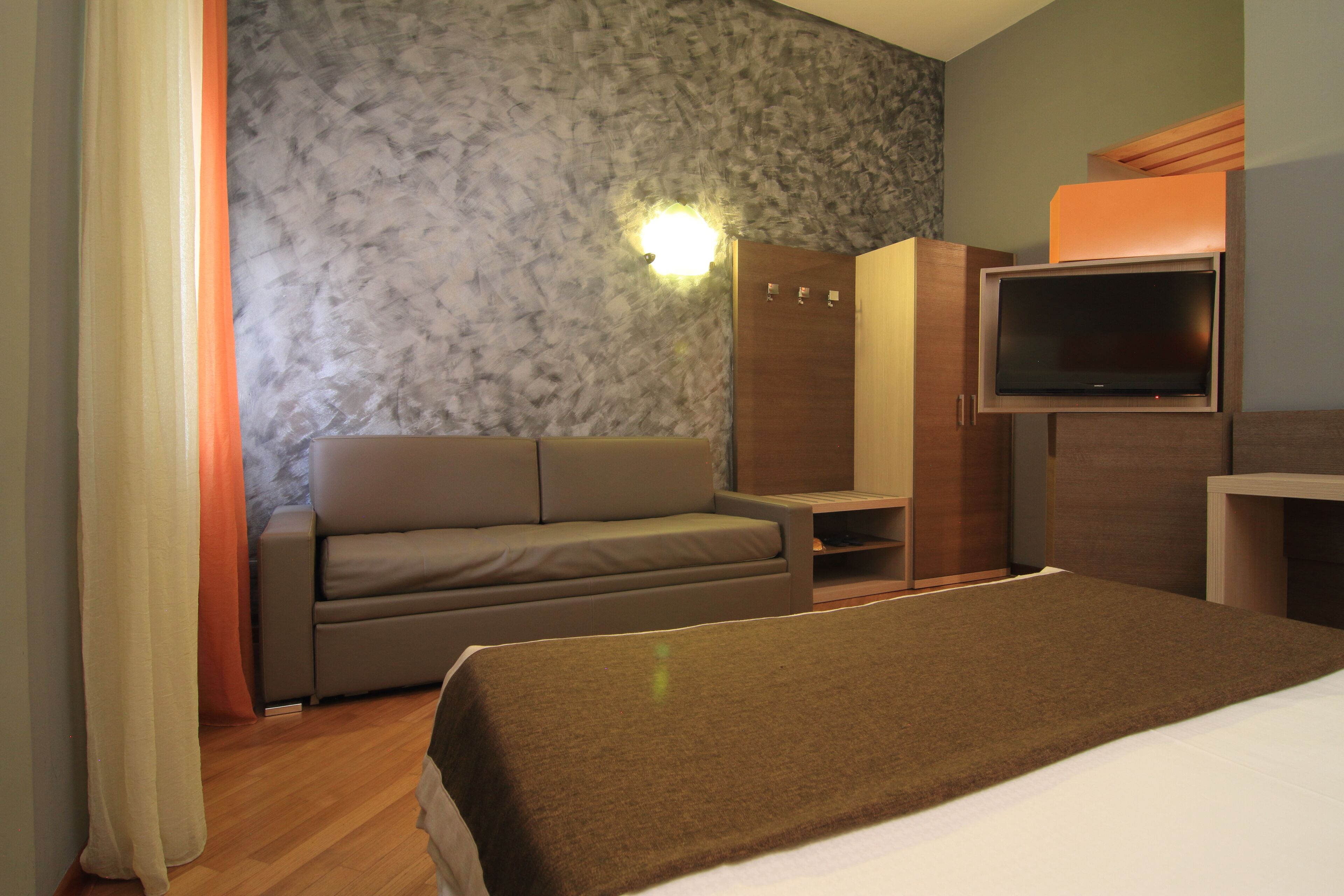 Habitació d'hotel amb un llit, un sofà, una televisió i un armari.