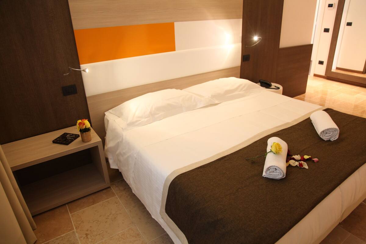 A hotel room with a bed, a bedside table, a nightstand, a phone, and a decorative flower arrangement.