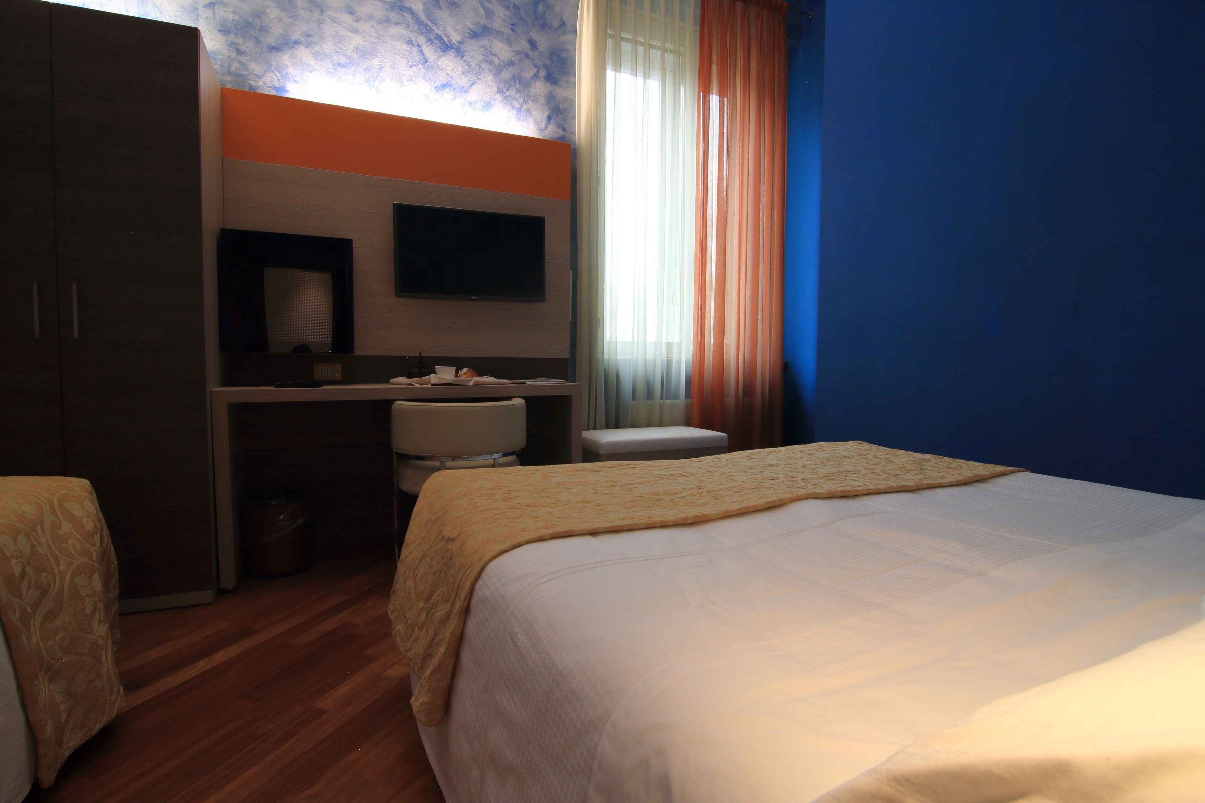 A hotel room with a bed, a desk with a chair, a television, and a window with curtains.