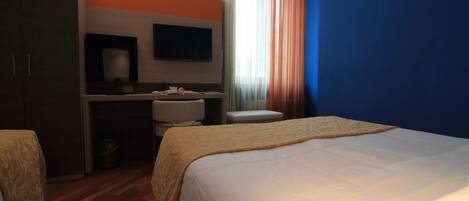 A hotel room with a bed, a desk with a chair, a television, and a window with curtains.
