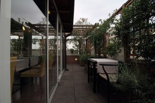 An outdoor patio with wooden flooring, tables, chairs, and a glass enclosure.