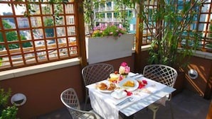 A balcony with a table set for a meal, surrounded by chairs, and a view of the cityscape through a wooden lattice. - Hotel Metro (Milan)