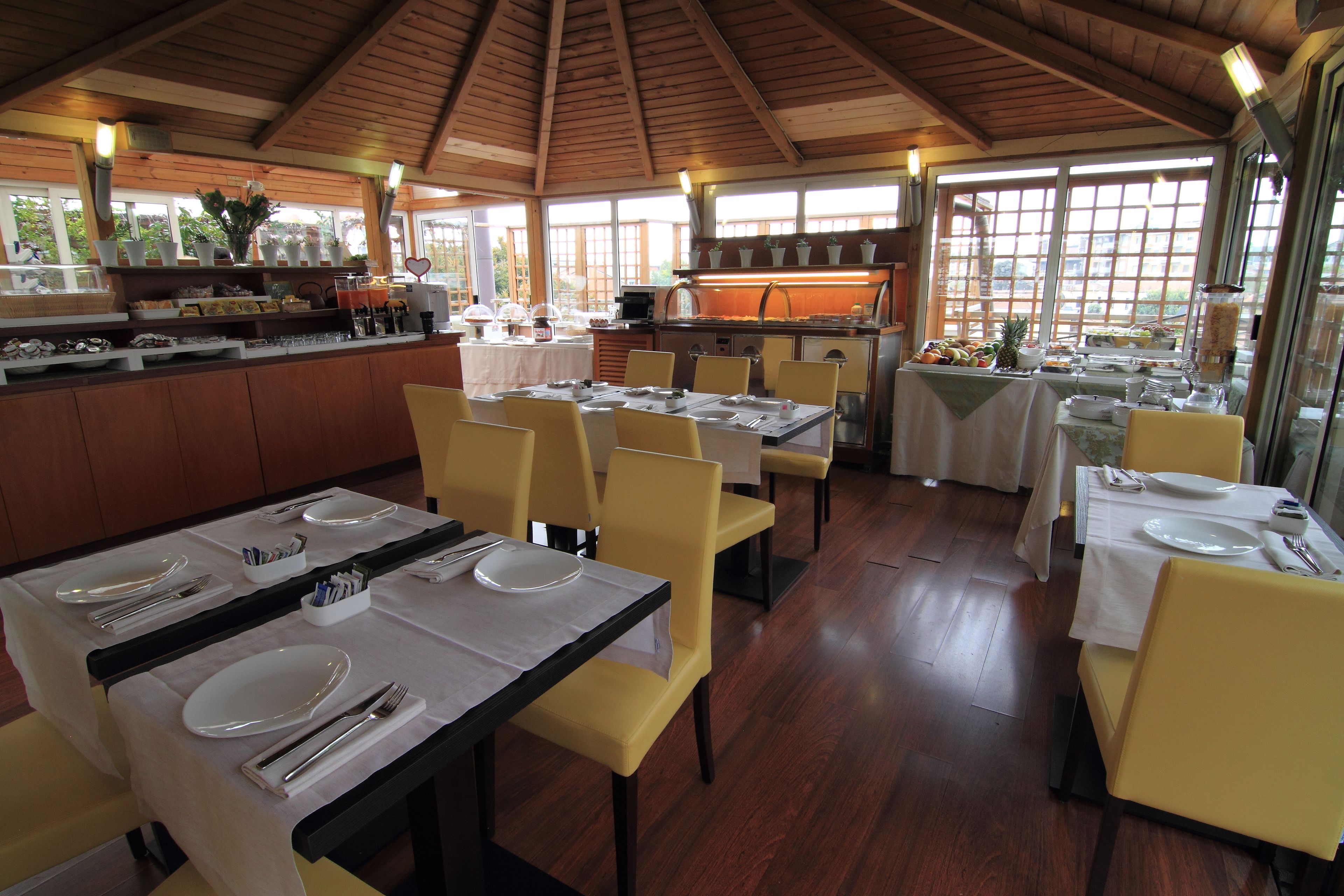 A restaurant with multiple tables set for dining, a kitchen area, and large windows allowing natural light.