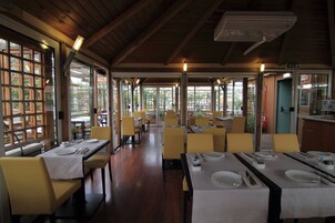 A restaurant with wooden beams, large windows, and yellow chairs. Tables are set with white tablecloths and silverware.