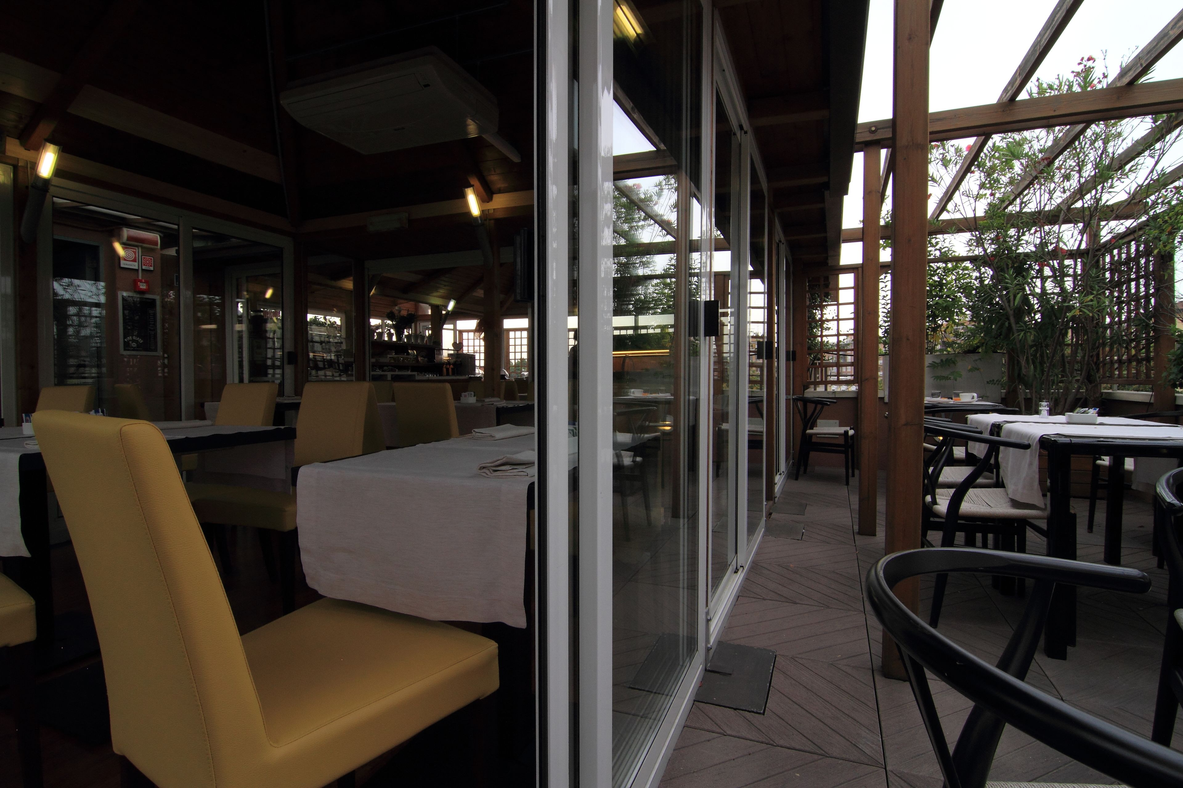 Un restaurante al aire libre con mesas y sillas, cubierto por un techo y amplias ventanas.