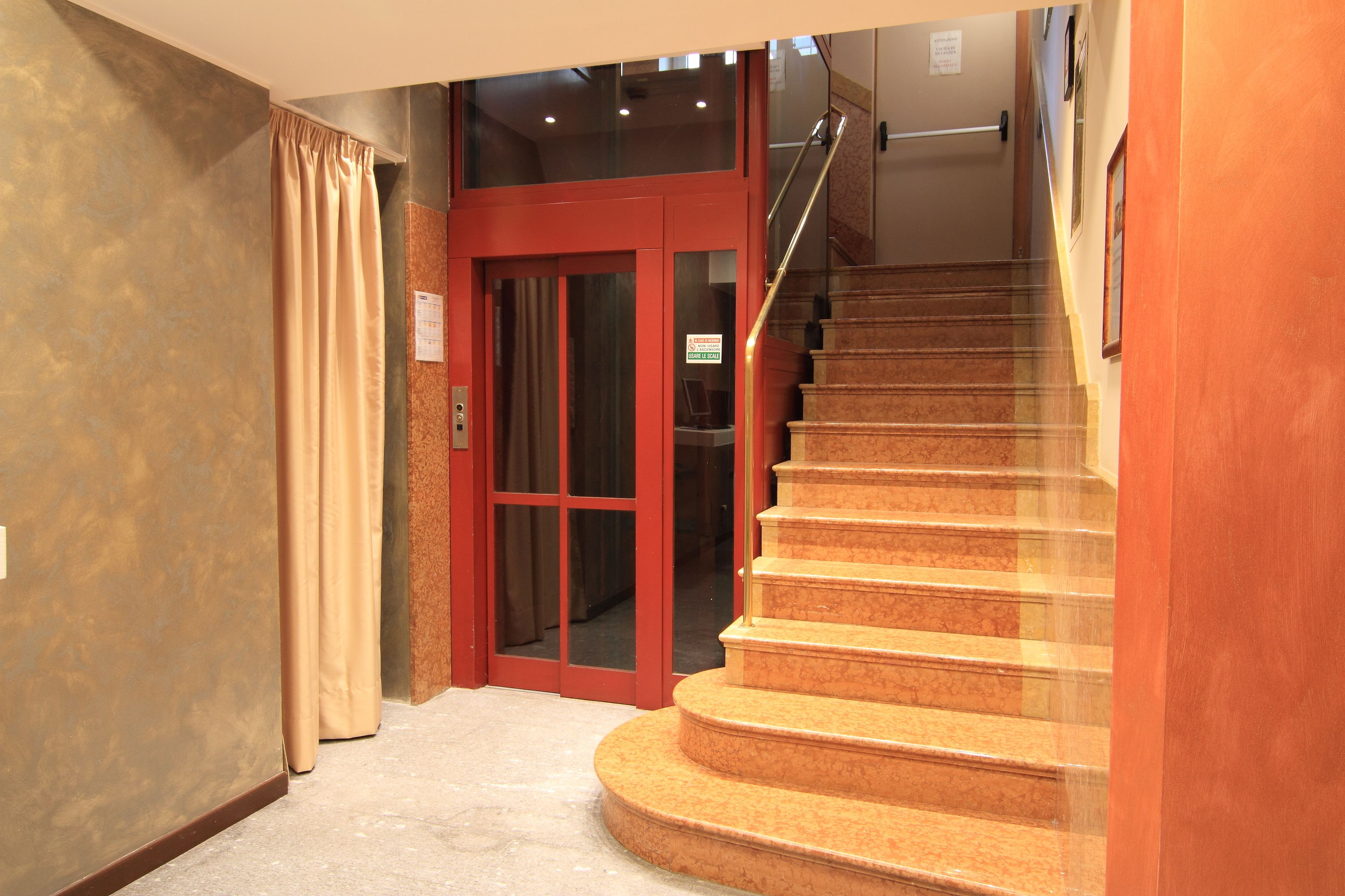 A hotel interior with a staircase leading to an upper floor, a red door, and a sign indicating a smoking area.