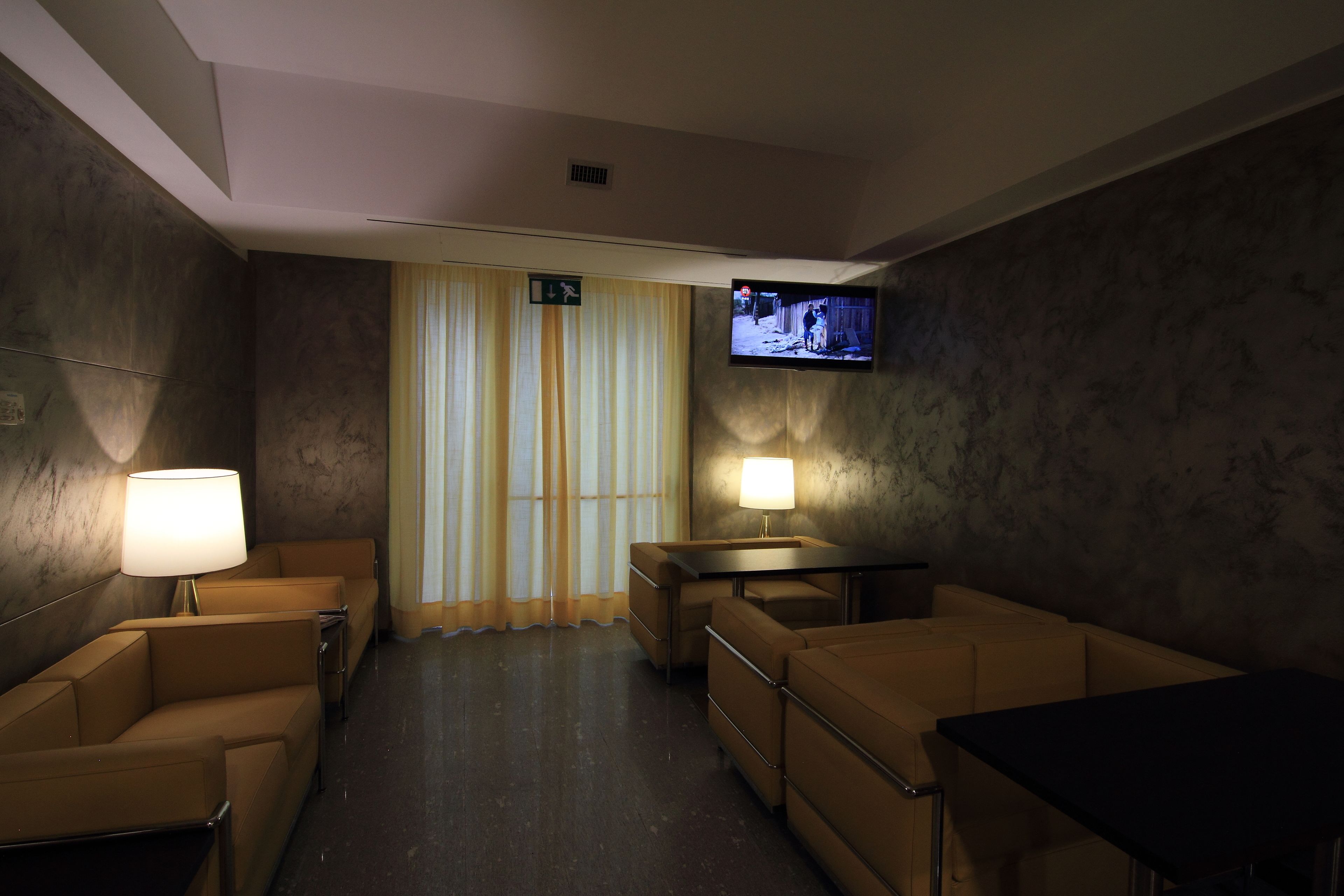 Ein Hotelzimmer mit einer Couch, einem kleinen Tisch, einem an der Wand befestigten Fernseher und einer Lampe auf der linken Seite.