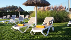 A poolside area with lounge chairs, a thatched umbrella, and a small table with a glass of wine. - Apartamentos Sol Romántica by DOT Suites (Manacor)