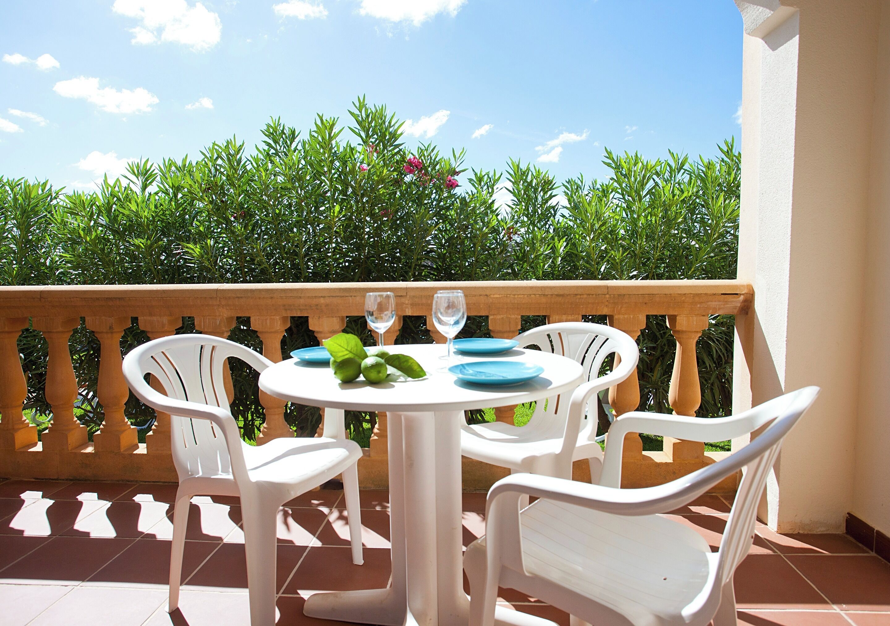 Een ronde tafel met witte stoelen op een balkon, omgeven door groene planten.