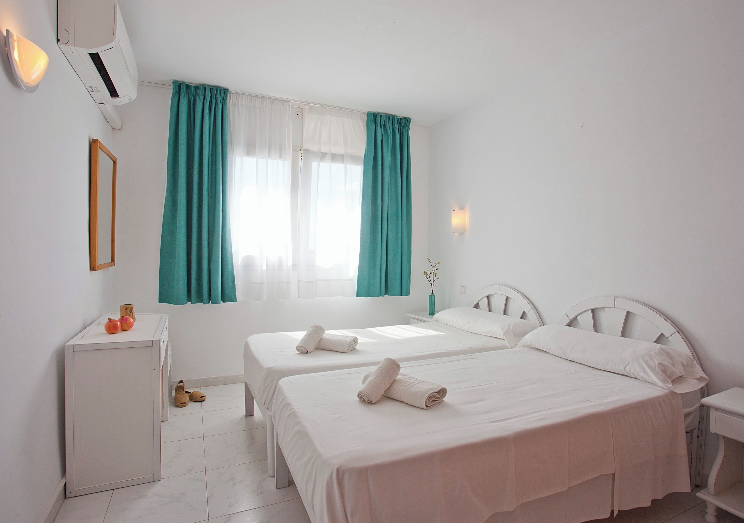 Een hotelkamer met twee bedden, een klein bureau en een raam met gordijnen.